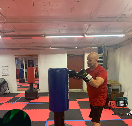 man punching blue boxing bag with black gloves